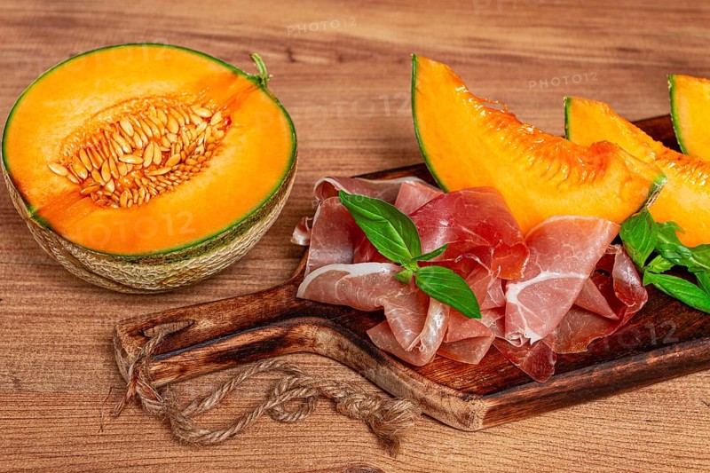 Cantaloupe melon, with prosciutto, and fresh basil, on a wooden serving board, rustic style