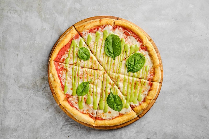 Mouthwatering pizza features a golden crust topped with rich tomato sauce, melted cheese, and fresh spinach leaves drizzled with a vibrant green sauce. Perfect for a casual meal at any time