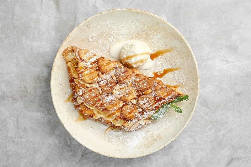 A beautifully plated dessert showcases a crispy pastry filled with caramelized bananas, dusted with powdered sugar and accompanied by a scoop of vanilla ice cream, perfect for any sweet lover