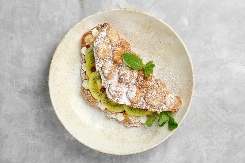 A delightful dessert featuring a crispy pastry shell filled with sliced kiwi, topped with powdered sugar and fresh mint. Enjoyed in a cozy cafe setting during a mid-afternoon treat