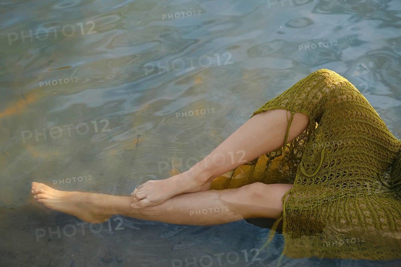 On a warm day, a person relaxes by the lake, dipping her feet into the clear water. Sunlight dances on the surface, creating a tranquil atmosphere ideal for summer enjoyment and relaxation