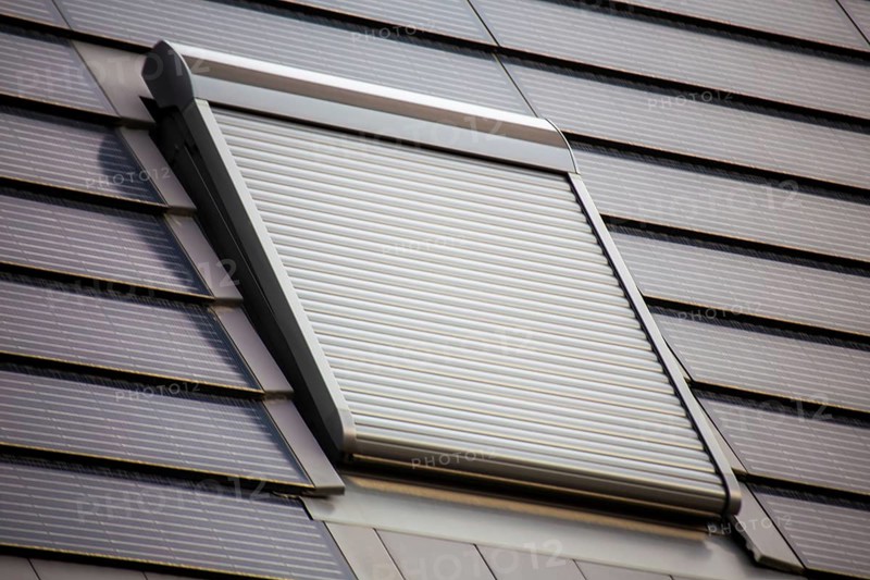 Roof window with roller shutter on a roof covered with solar tiles