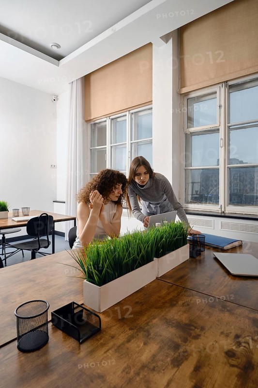 In a modern workspace, two women engage in a focused discussion about women's health initiatives. They share ideas while examining documents and prototype application