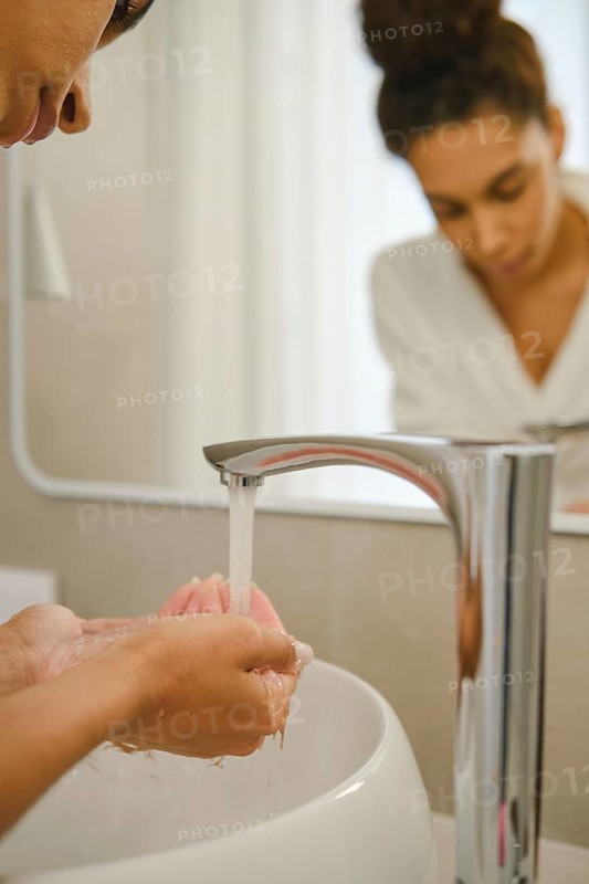 In a contemporary bathroom, a woman is washing her hands under a sleek faucet. She focuses on her hygiene while preparing for her day. Natural light fills the space, creating a serene atmosphere
