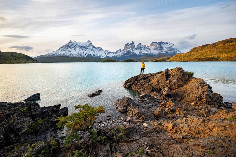 Young man on the shore of the blue lake Lago Pehoe in the evening light, Cuernos del Paine mountain range, Torres del Paine National Park, Chile