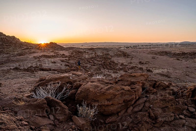 Photographer in desert landscape at sunrise with sun star, Erongo, Damaraland, Namibia