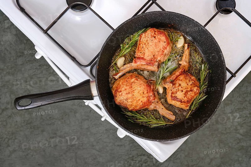 Pork rib roast sizzles in a skillet on the stovetop, surrounded by fragrant garlic and fresh herbs. The rich aroma fills the kitchen while the meat cooks to perfection