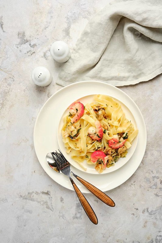 Delicious fettuccine allo Scoglio features an array of seafood mixed with pasta, presented elegantly on a white plate. A cozy dining atmosphere is enhanced by simple cutlery and salt shakers