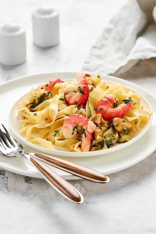 A delectable portion of fettuccine allo scoglio sits elegantly on a white plate. The dish features seafood such as shrimp and mussels, garnished with fresh herbs