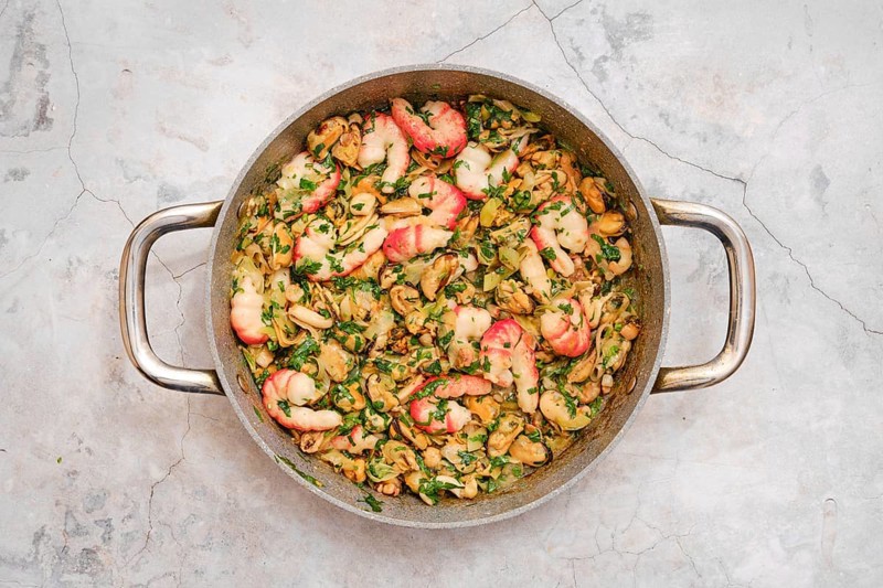 Seasoned ingredients allo scoglio features an assortment of seafood, including shrimp and clams, tossed with fresh herbs, and served in a rustic stainless steel pan