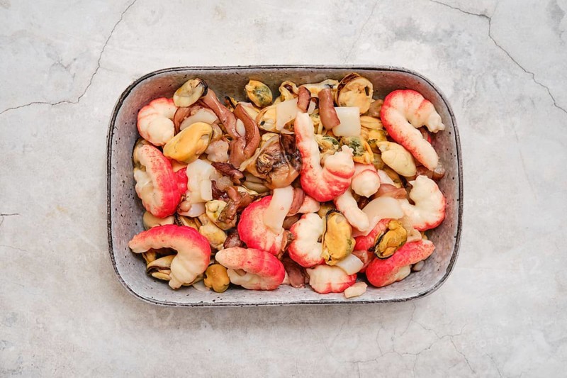 Overhead view of a bowl with shrimps, mussels, and squid. The dish showcases vibrant colors and fresh ingredients, perfect for a flavorful experience by the coast at dinner time