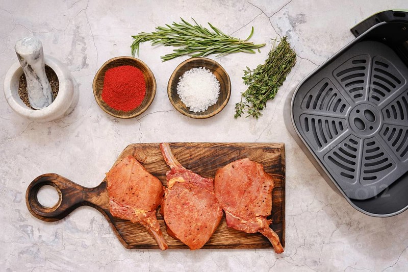 Marinated pork rib roast is seasoned with herbs and spices on a wooden cutting board while being prepared for cooking in an air fryer