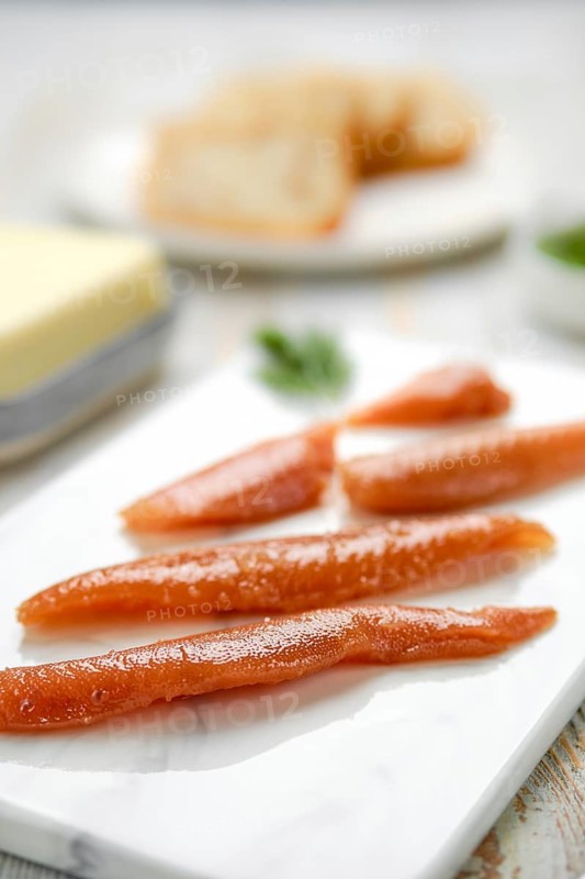 Herring caviar glisten with a rich color, artfully arranged on a marble platter. In the background, slices of butter and herbs hint at a culinary preparation