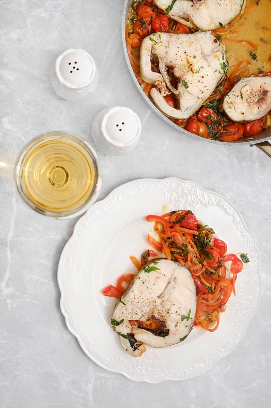 Tender cod fish fillet with colorful sautéed peppers, carrots and tomatoes on a plate on a dining table