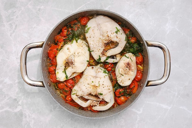 Cod fish fillets are gently simmering in a tangy tomato sauce, accompanied by vibrant cherry tomatoes and fresh herbs