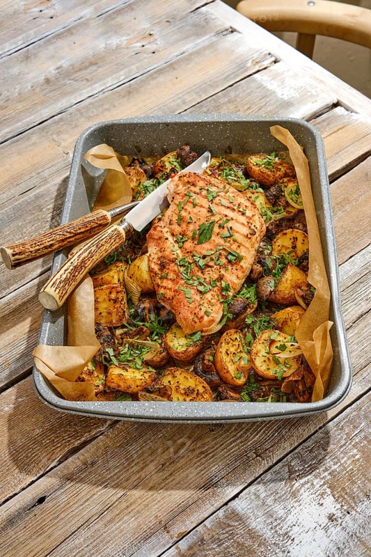 A succulent roasted turkey breast sits atop a bed of roasted golden potatoes, garnished with fresh herbs, creating a hearty meal on a rustic wooden table in a cozy setting