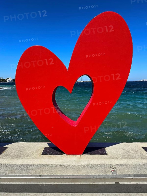 Red heart sculpture in front of blue sea and sky, romantic modern art on concrete base, Kos Town, Kos, Dodecanese, Greek Islands, Greece