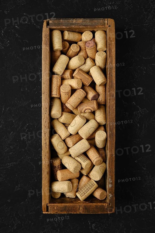 A wooden box is filled with an assortment of wine corks, showcasing various shapes and textures