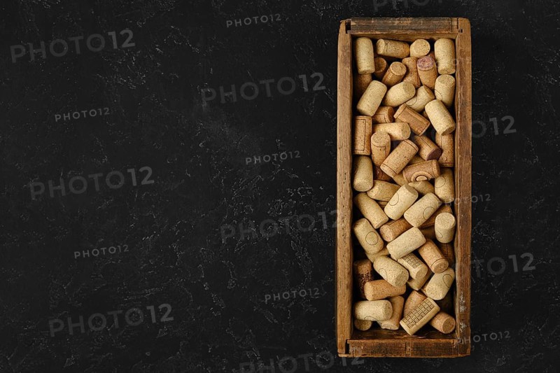 A wooden box filled with assorted wine corks rests on a dark surface. The corks vary in size and shape, showcasing a collection from different wine bottles, hinting at past wine tastings