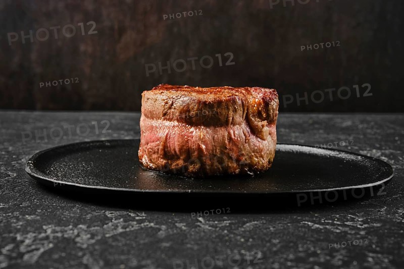 A perfectly cooked filet mignon rests on a sleek black plate, showcasing its rich color and delicate texture