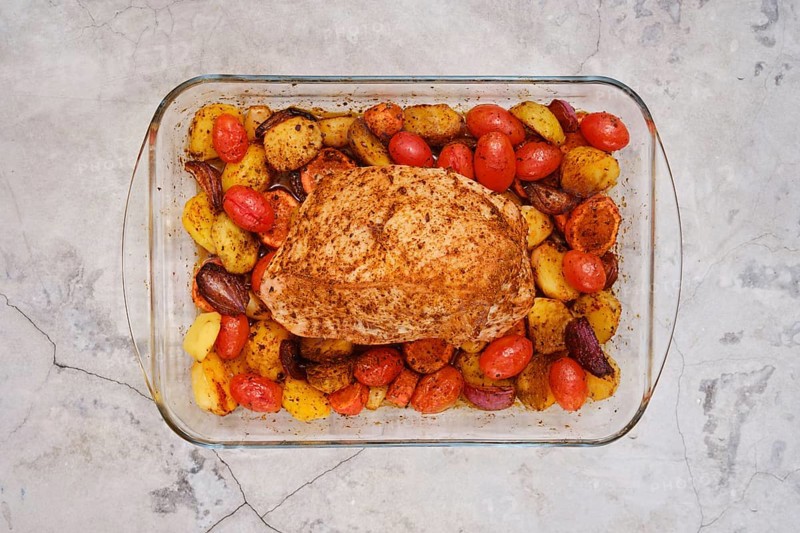 Juicy turkey breast seasoned with spices rests atop a bed of roasted baby potatoes, cherry tomatoes, and carrots. The dish is oven-cooked for a flavorful and colorful meal ready to serve