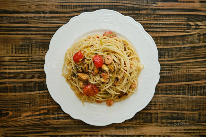 A generous serving of spaghetti topped with an assortment of seafood, including shrimp and mussels, garnished with fresh cherry tomatoes and herbs, elegantly presented on a white plate