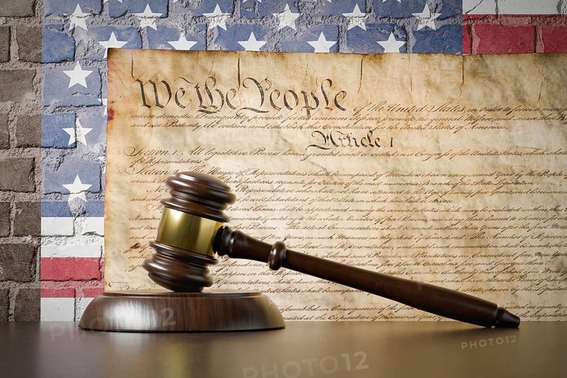 United states constitution and american flag on wall with gavel resting on table in front