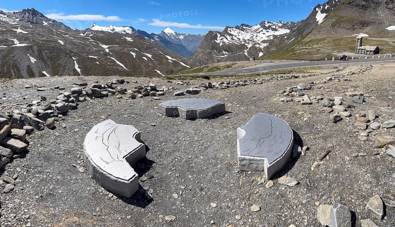 In front three orientation boards on stone for landscapes and mountain peaks at viewpoint next to highest asphalted pass Col d'iseran Pass in Alps High Alps above tree line behind view of mountain landscape with high peaks, Route des Grandes Alpes, Département Savoie, Region Auvergne-Rhône-Alpes, Graian Alps, France