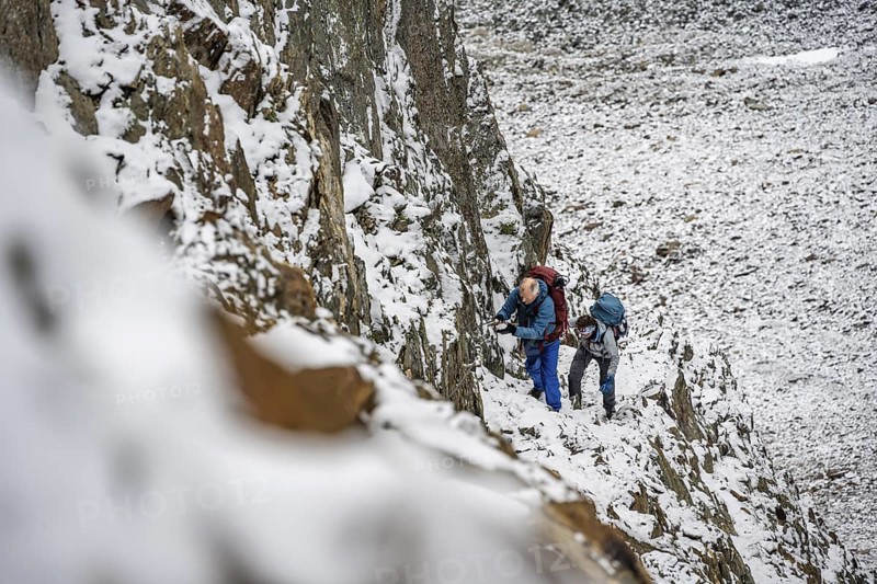 Mountaineer on a rope-secured path in a steep, rocky mountain landscape with fresh snow in summer, ascent to the Hornscharte, Schober Group, Hohe Tauern National Park, Carinthia, Austria