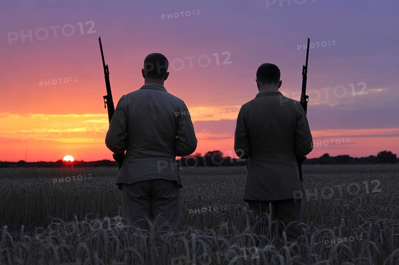 Back view of two soldiers standing in grain field watching sunset. Captures moment of reflection and calm amid nature. Generative ai, AI generated