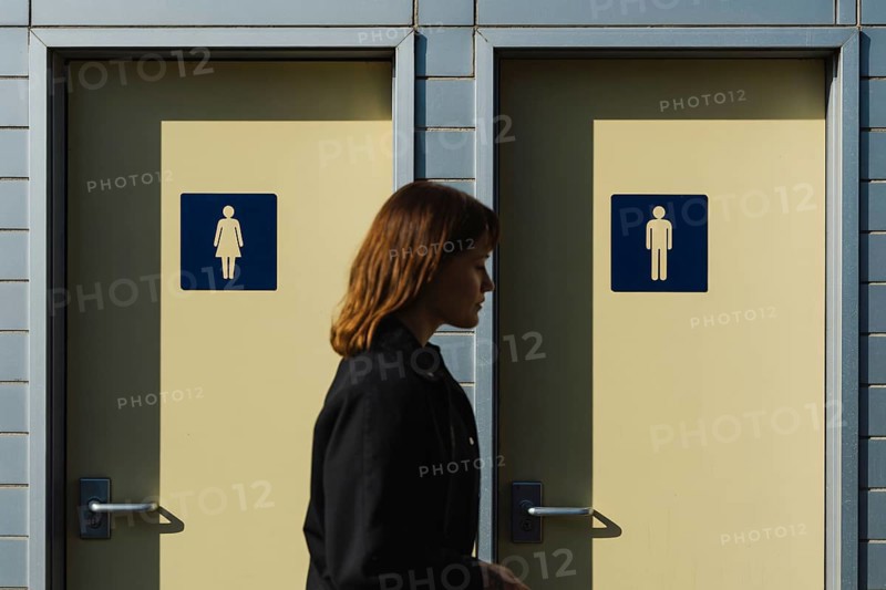 Transgender woman in front of men's and women's bathroom doors. Concept of public restroom access and trans rights debate. Generative ai, AI generated