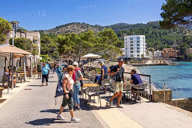 Tourists on a boardwalk and restaurants by the Mediterranean Sea at a tourist resort a sunny summer day, Sant Elm, Mallorca, Spain