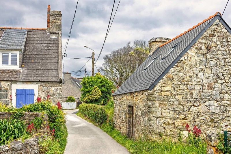 Alley in an old French village with old stone houses with flowers in bloom in the countryside a summer day, Crozon peninsula, Bretagne, France
