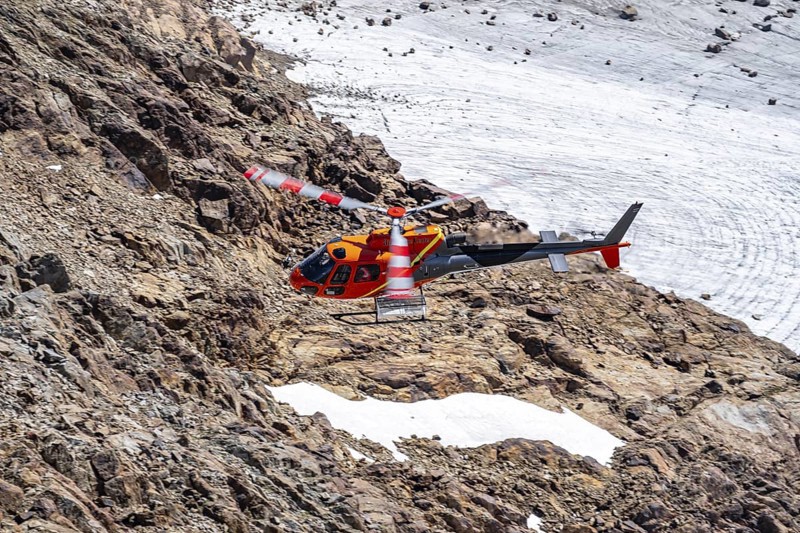 Red helicopter flies over glaciers in the mountains, Stubai Alps, South Tyrol, Italy