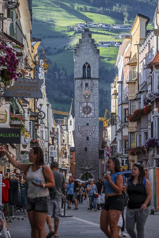 Tourists in the old town, colourful houses in the main street, Zwölferturm tower at the back, Sterzing, South Tyrol, Italy