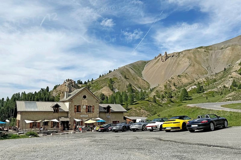 View of historic inn Refuge Napoleon on north ramp northern ascent downhill mountain road in front of pass summit of Alpine pass road Col d'Izoard, in front of it on the right many Porsche sports cars, Col de l'Izoard, Cottian Alps, Route des Grandes Alpes, Département Hautes-Alpes, France