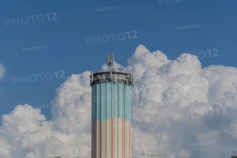 A tall water tower, painted in bright colours, rises against a backdrop of flowing white clouds. The clear blue sky enhances the vibrant colours of this building in a peaceful suburban landscape. Bas rhin, Alsace, grand est, France