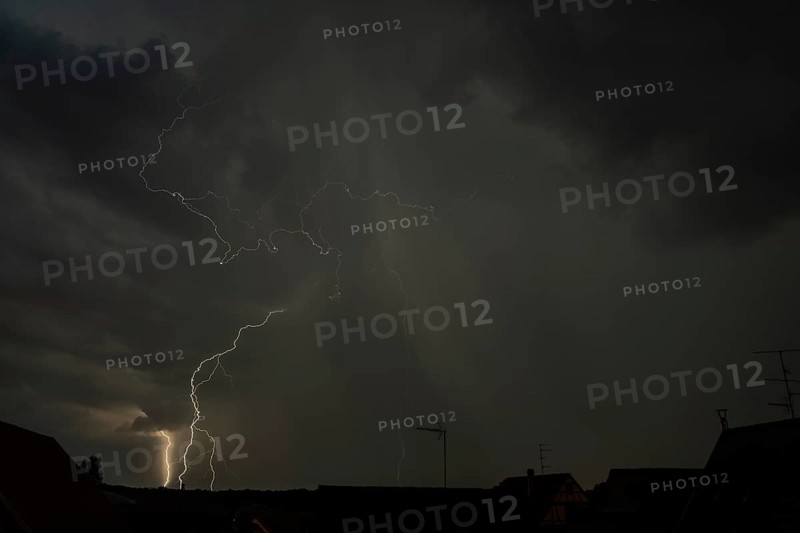 Dark clouds gather as lightning strikes light up the night above the rooftops. The intense storm brings thunder and rain to the quiet neighbourhood below. Bas rhin, Alsace, grand est, France