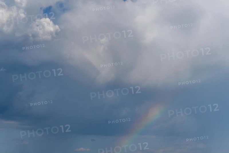Bright sunlight breaks through large clouds after a rain shower and reveals a magnificent rainbow across the sky. The serene landscape below adds to the picturesque moment. Bas rhin, Alsace, grand est, France