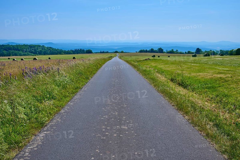 Straight road through a vast landscape of green meadows and distant hills under a blue sky, Koppelhutweg, Lange Rhön, Hausen, Rhön, Bavaria, Germany
