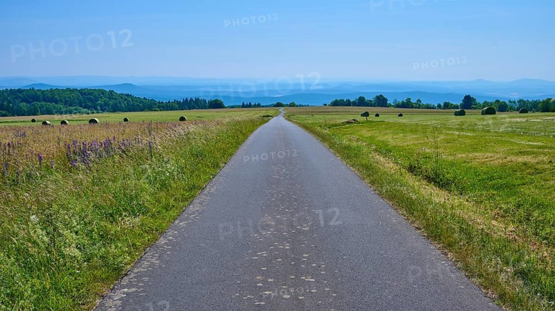 Endless road leads through green fields under a clear blue sky with hills in the distance, Koppelhutweg, Lange Rhön, Hausen, Rhön, Bavaria, Germany