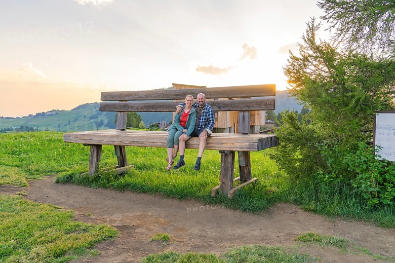A couple sits on an oversized bench and enjoys the sunset, Alpe di Siusi, Dolomites, South Tyrol, Italy