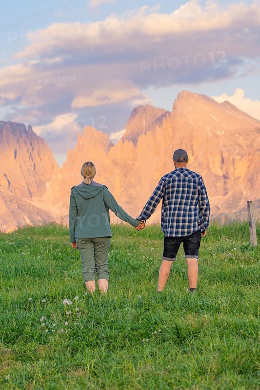 A couple holding hands in a meadow against an impressive mountain backdrop, Alpe di Siusi, Dolomites, South Tyrol, Italy
