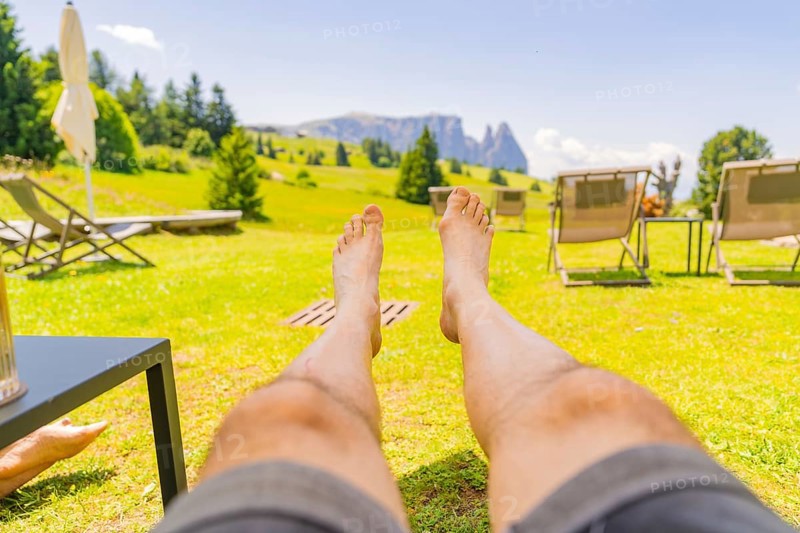 Person lying in a deckchair enjoying the summer landscape and the peace and quiet in a meadow, Alpe di Siusi, Dolomites, South Tyrol, Italy