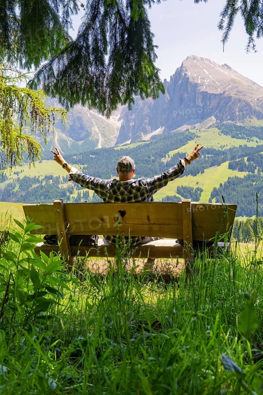 Person on a bench with outstretched arms in front of a mountain landscape, Alpe di Siusi, Dolomites, South Tyrol, Italy