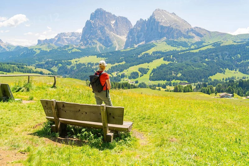 Person stands next to a bench and enjoys the view of the mountains, Alpe di Siusi, Dolomites, South Tyrol, Italy
