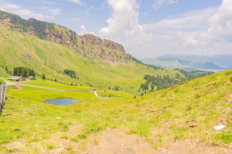 Green valley with hills and a road under a blue sky, Alpe di Siusi, Dolomites, South Tyrol, Italy
