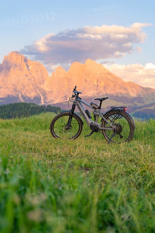 A bicycle stands in a meadow in front of an impressive mountain landscape at sunset, Alpe di Siusi, Dolomites, South Tyrol, Italy