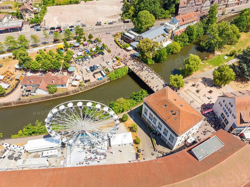 View from above of a summer festival with Ferris wheel, bridge and many people along a river in the city centre, 950 years Calw, parade Calw, Black Forest, Germany