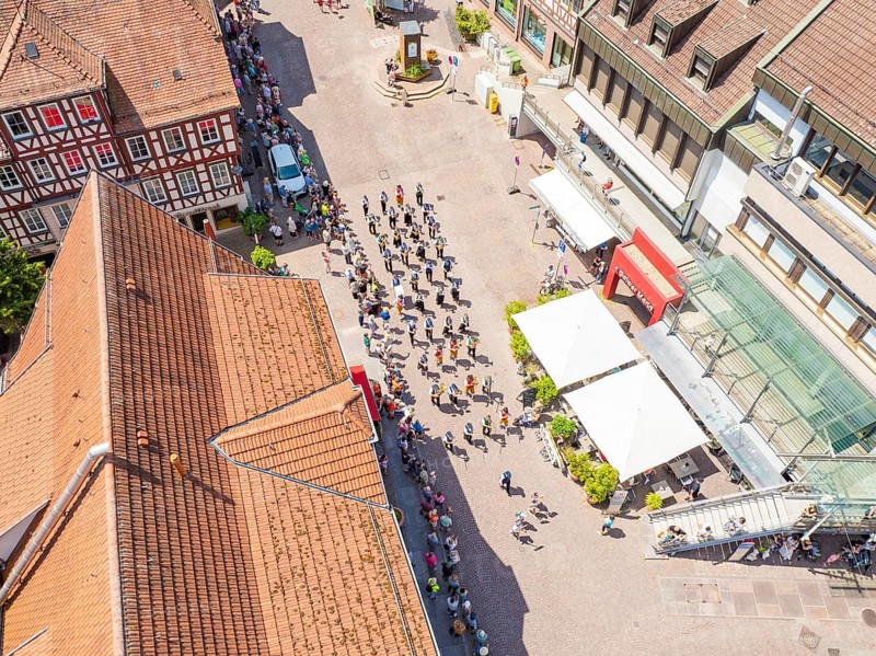 Aerial view of a parade through the centre of a sunny half-timbered town with crowds of people, 950 years of Calw, Calw parade, Black Forest, Germany